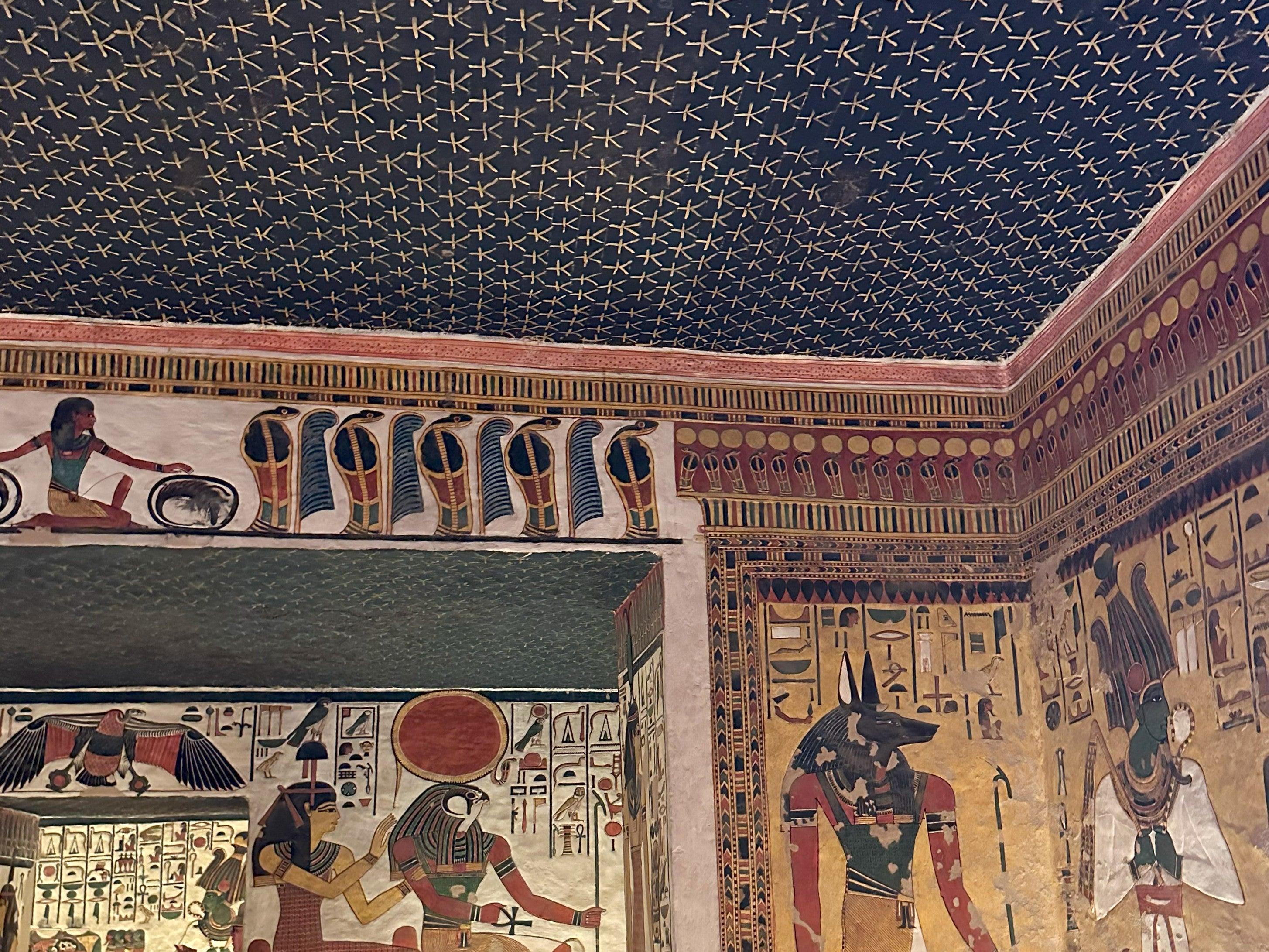 Tomb chamber corner showing Anubis and deities beneath a gold-starred ceiling.