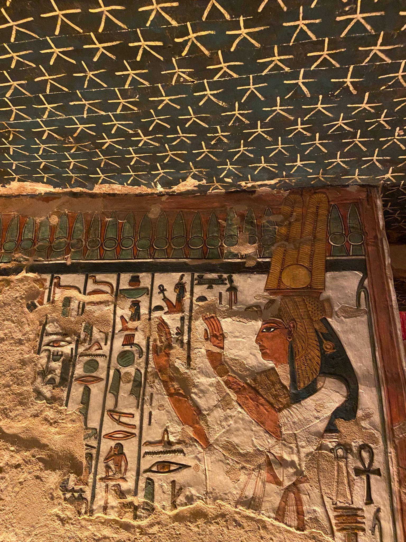 Painted relief of a goddess wearing tall plumed headdress beside hieroglyph columns.