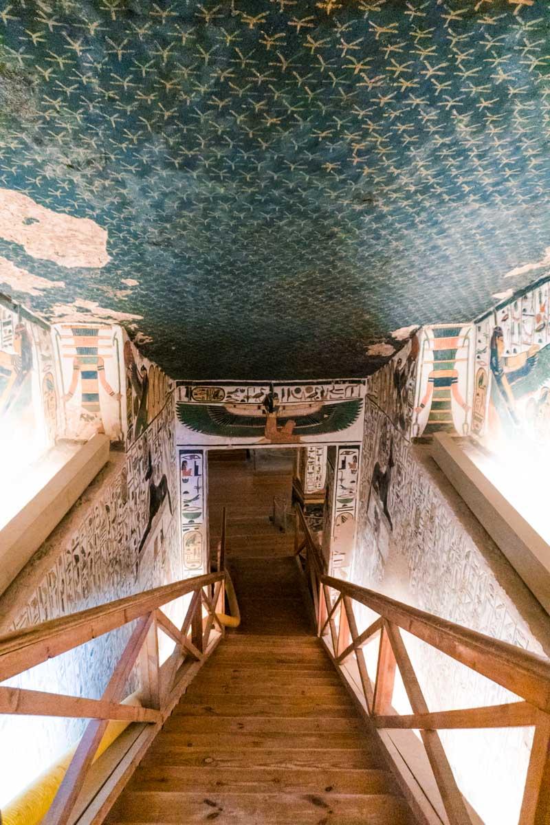 Wooden stairway descending into a painted tomb corridor with starry ceiling.