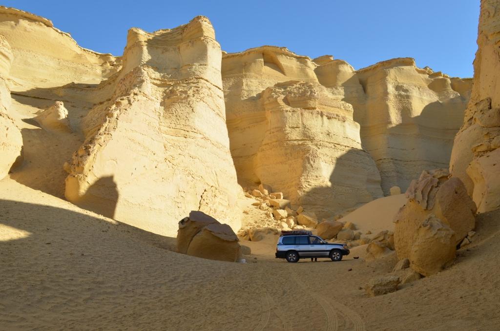 Four-wheel-drive parked beneath towering sandstone cliffs in the desert of Wadi Al-Hitan, Fayoum