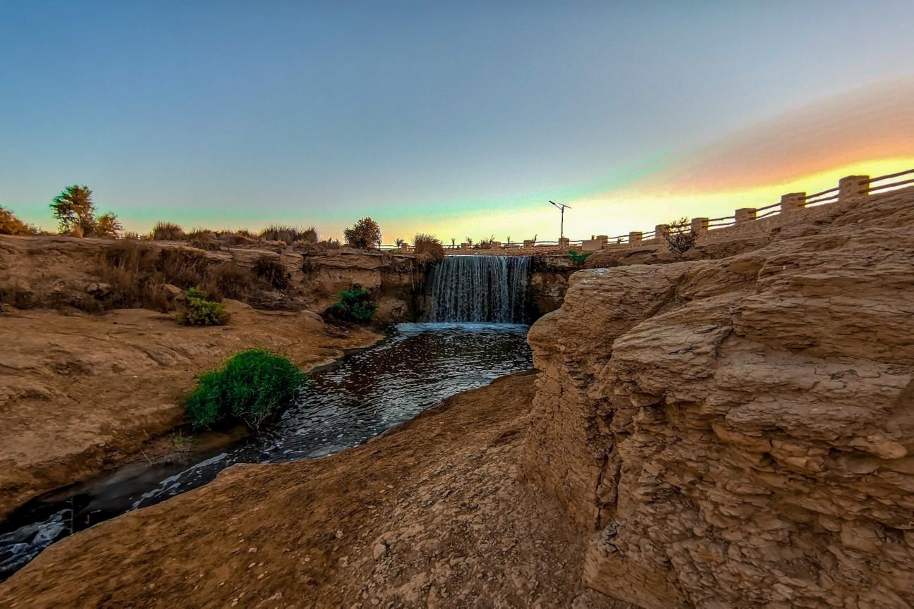 Small desert waterfall glowing under a soft pastel sunset sky